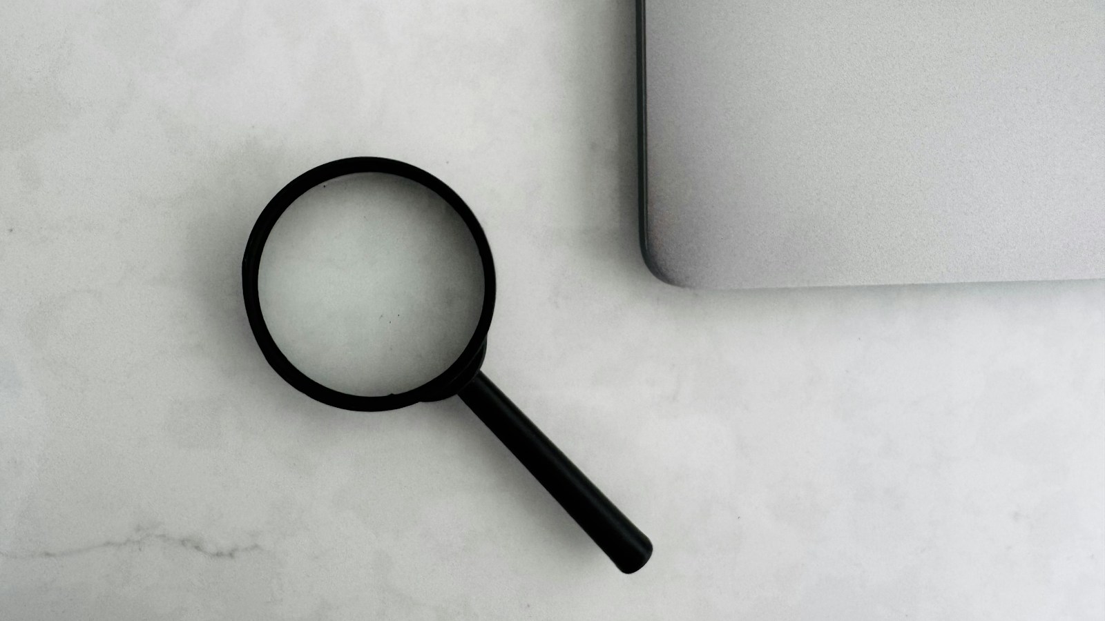 A magnifying glass beside a laptop on a table
