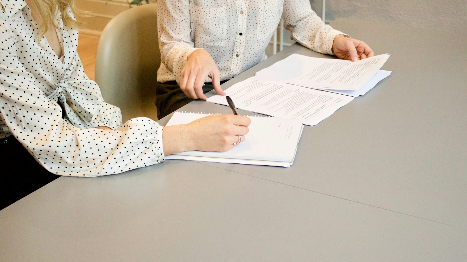 A woman signing on white printer paper beside another woman