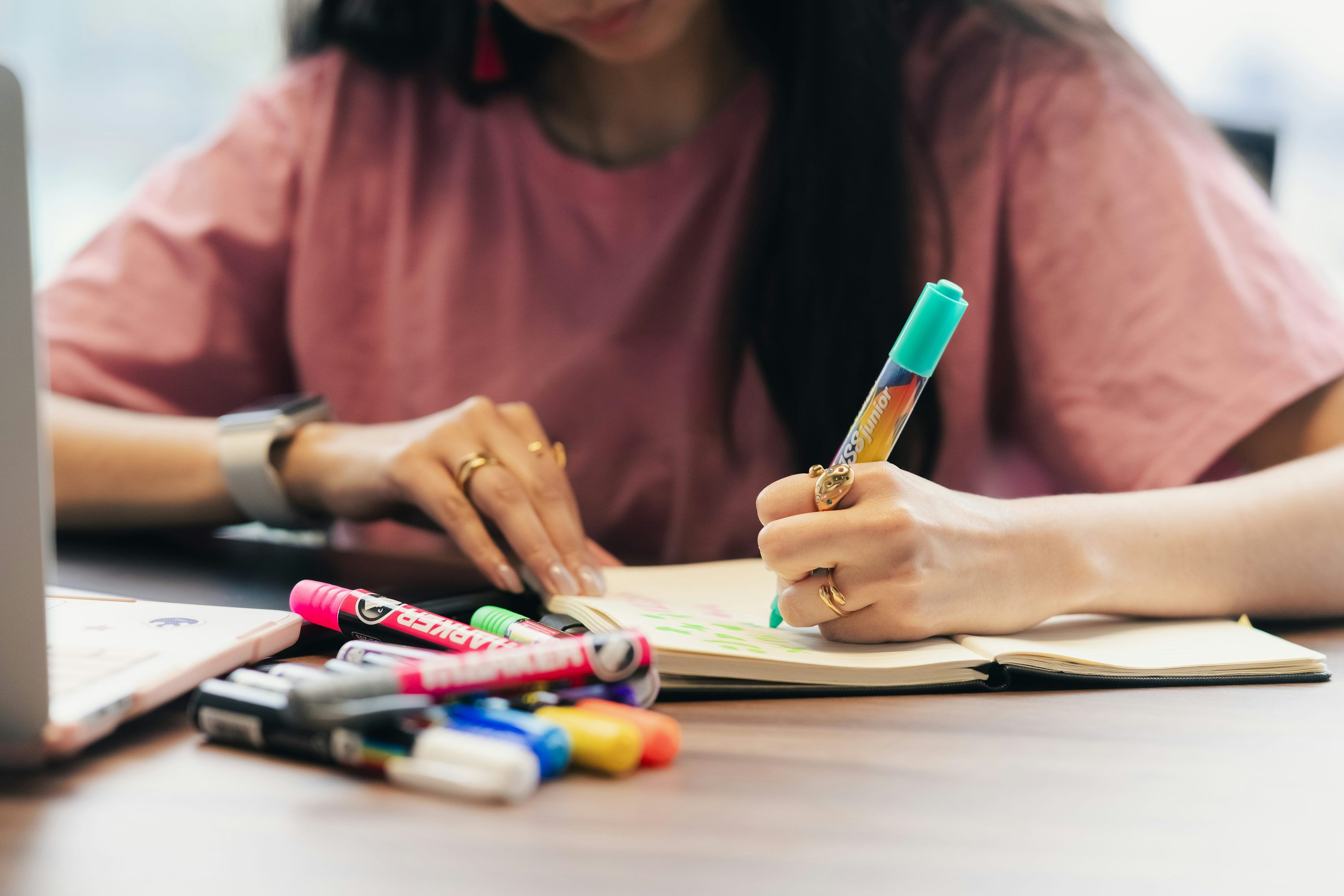 A writer working in a notebook with colored pens nearby.
